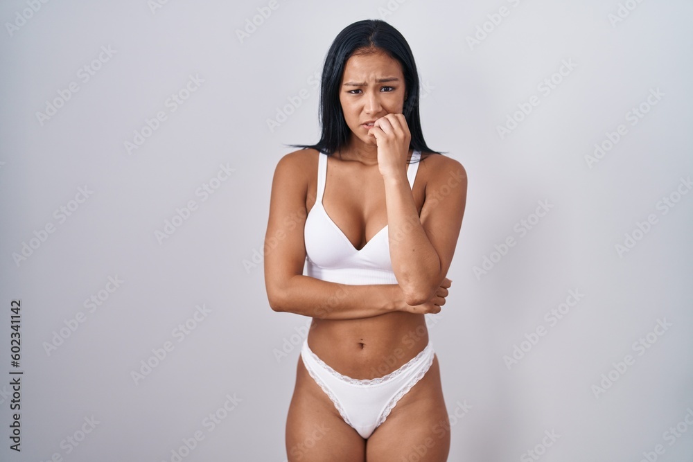 Hispanic woman wearing lingerie looking stressed and nervous with hands on mouth biting nails. anxiety problem. - obrazy, fototapety, plakaty 