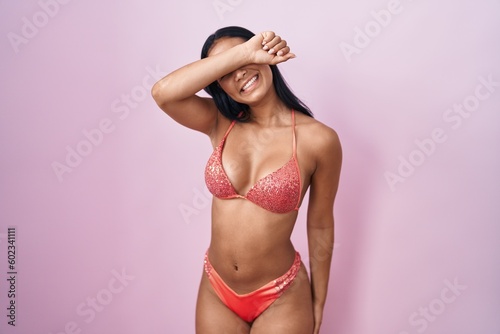 Hispanic woman wearing bikini covering eyes with arm smiling cheerful and funny. blind concept.