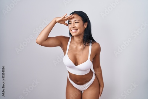 Hispanic woman wearing lingerie very happy and smiling looking far away with hand over head. searching concept. © Krakenimages.com