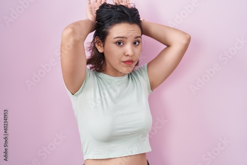 Hispanic young woman standing over pink background doing bunny ears gesture with hands palms looking cynical and skeptical. easter rabbit concept.