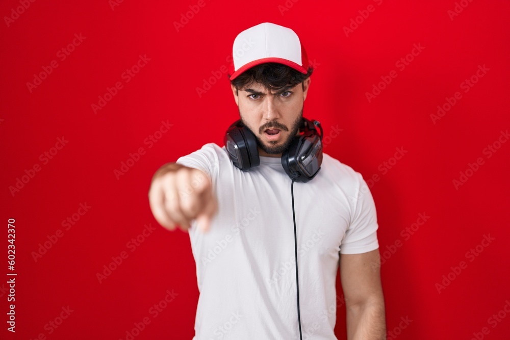 Hispanic man with beard wearing gamer hat and headphones pointing displeased and frustrated to the camera, angry and furious with you Hispanic man with beard wearing gamer hat and headphones pointing displeased and frustrated to the camera, angry and furious with you