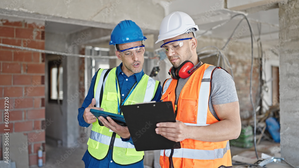 Two men builders reading document using touchpad shake hands at construction site