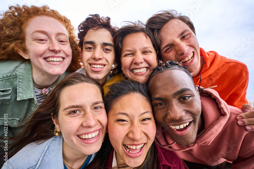 Multi-ethnic group smiling generation z boys and girls taking selfie outdoors. Happy lifestyle concept of friendship in multicultural young people having fun day together. Partners enjoying weekend. 