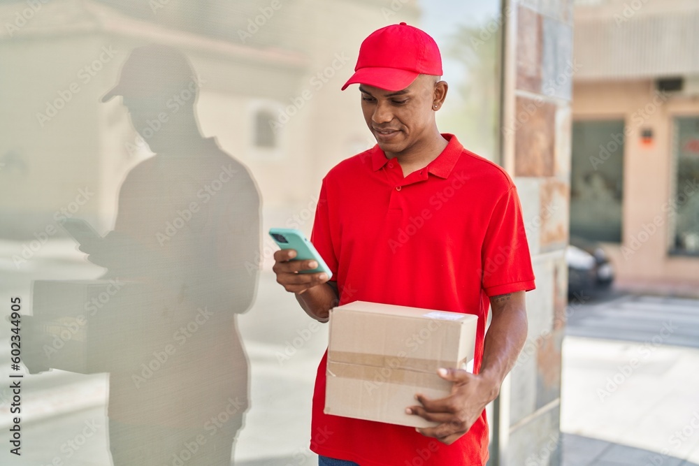 Young latin man delivery worker holding package using smartphone at street Young latin man delivery worker holding package using smartphone at street