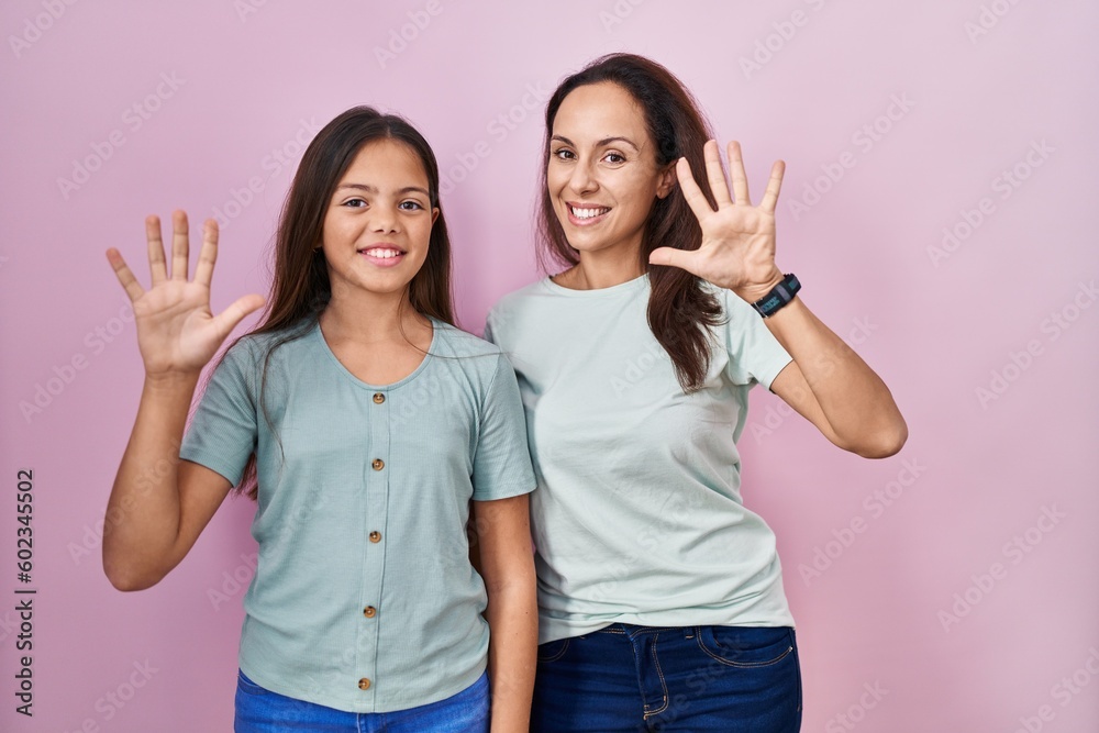 Young mother and daughter standing over pink background showing and pointing up with fingers number ten while smiling confident and happy. Young mother and daughter standing over pink background showing and pointing up with fingers number ten while smiling confident and happy.