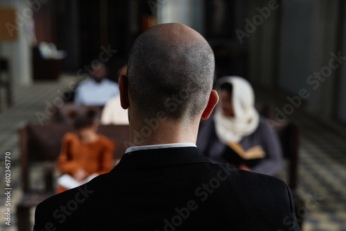 Rear view of protestant in black suit reading Bible for believers while they sitting on bench in baptist church