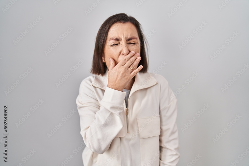 Middle age hispanic woman standing over isolated background bored yawning tired covering mouth with hand. restless and sleepiness. Middle age hispanic woman standing over isolated background bored yawning tired covering mouth with hand. restless and sleepiness.