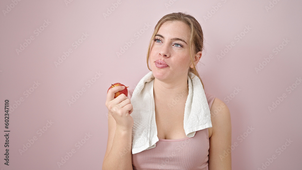 Young blonde woman wearing sportswear eating apple over isolated pink background Young blonde woman wearing sportswear eating apple over isolated pink background