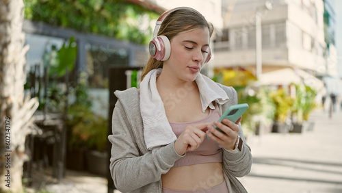 Young blonde woman wearing sportswear listening to music at street
