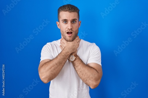 Fotografía Young caucasian man standing over blue background shouting suffocate because painful strangle