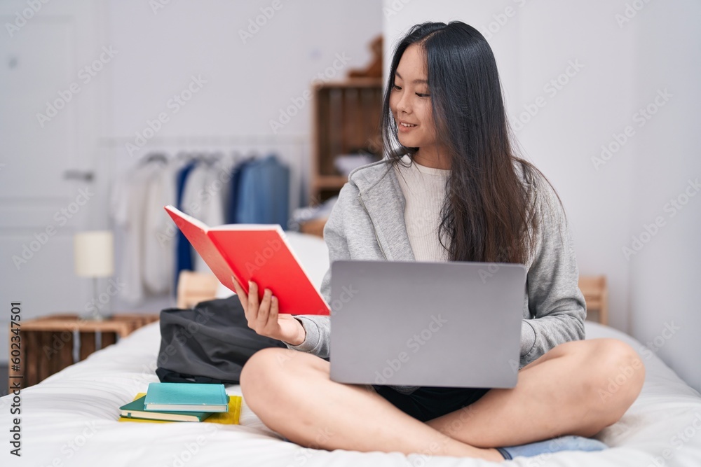 Young chinese woman using laptop reading notebook studying on bed at bedroom Young chinese woman using laptop reading notebook studying on bed at bedroom