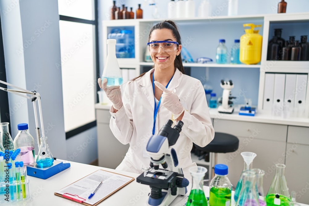 Hispanic woman working at scientist laboratory smiling happy pointing with hand and finger Hispanic woman working at scientist laboratory smiling happy pointing with hand and finger