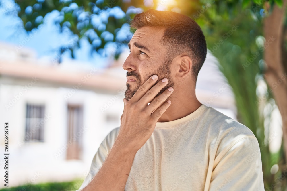 Young hispanic man standing with doubt expression at park