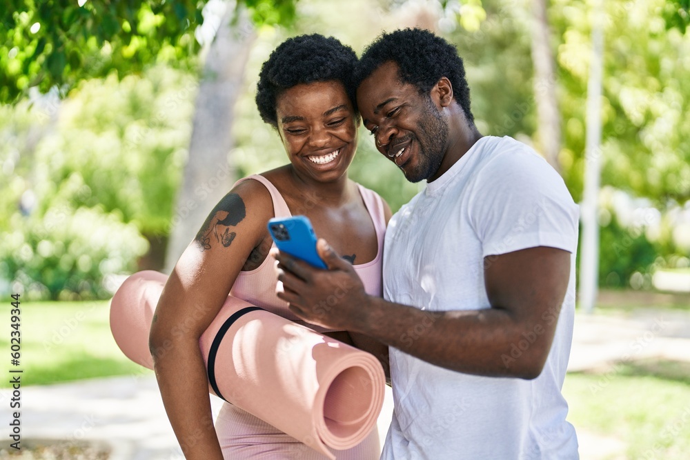 African american man and woman couple holding yoga mat using smartphone at park African american man and woman couple holding yoga mat using smartphone at park