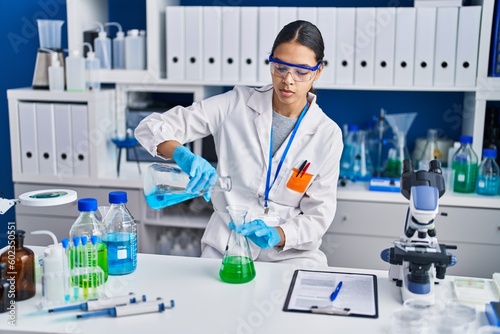 Young african american woman scientist pouring liquid at laboratory