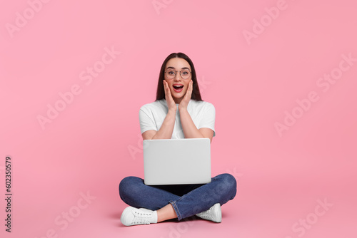 Surprised young woman with laptop on pink background