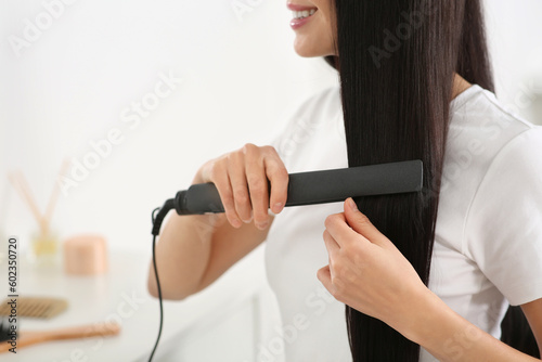 Happy woman using hair iron in room  closeup