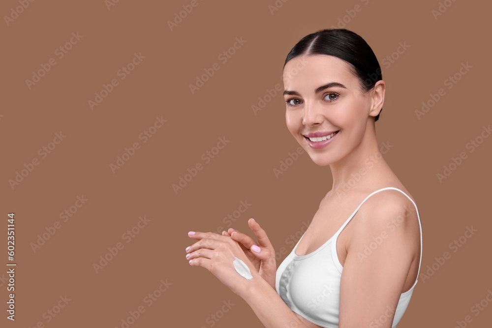 Beautiful woman with smear of body cream on her hand against light brown background, space for text Beautiful woman with smear of body cream on her hand against light brown background, space for text