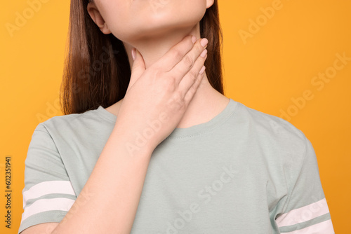 Woman with sore throat on orange background, closeup
