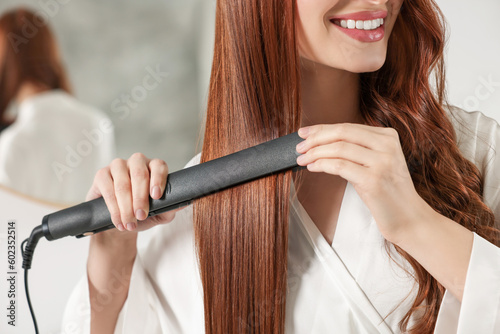 Young woman using hair iron indoors, closeup photo