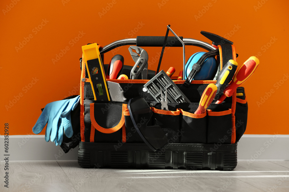 Bag with different tools for repair on floor near orange wall