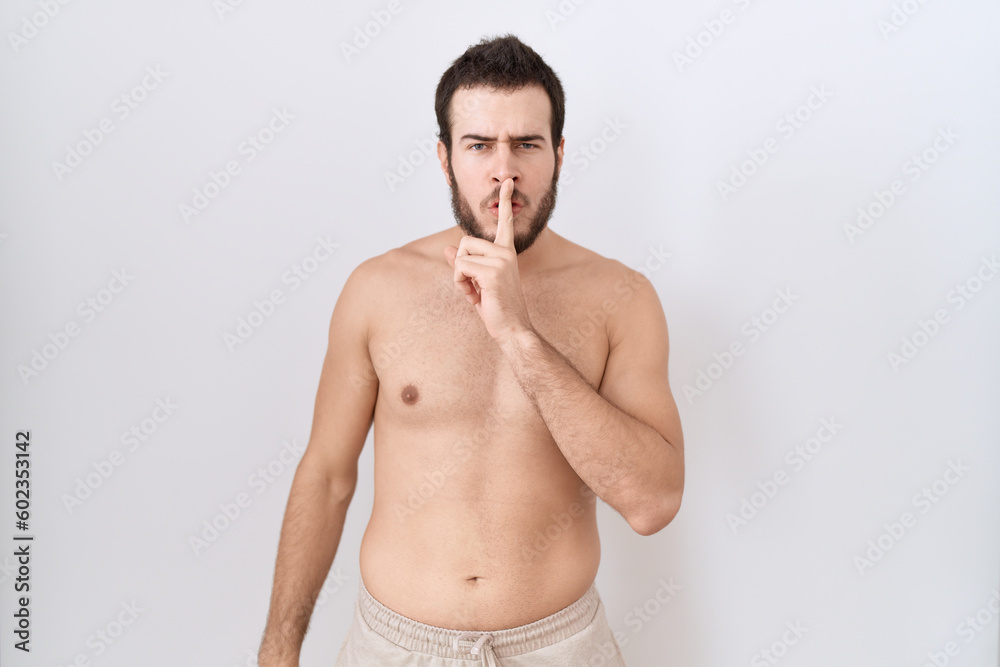 Young hispanic man standing shirtless over white background asking to be quiet with finger on lips. silence and secret concept.