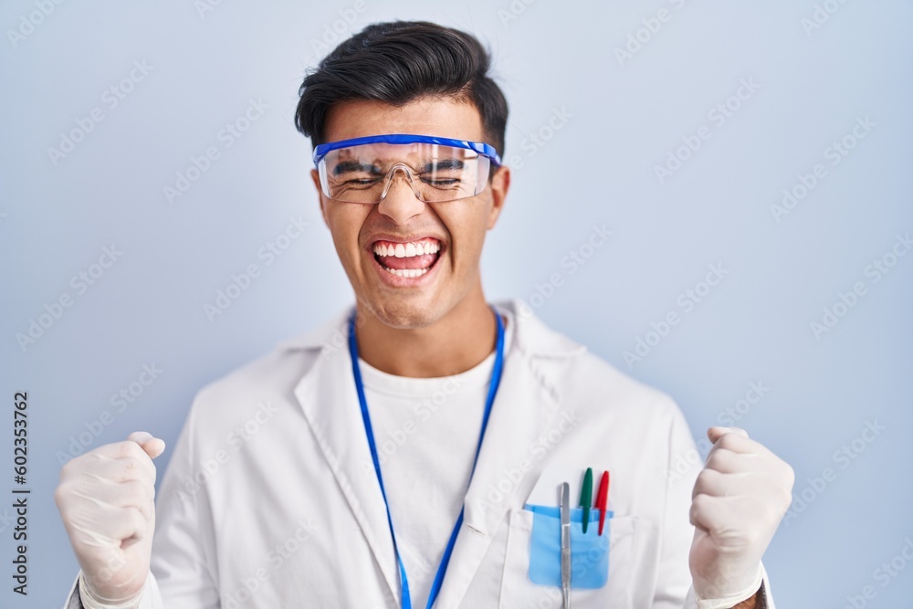 Hispanic man working as scientist excited for success with arms raised and eyes closed celebrating victory smiling. winner concept. Hispanic man working as scientist excited for success with arms raised and eyes closed celebrating victory smiling. winner concept.