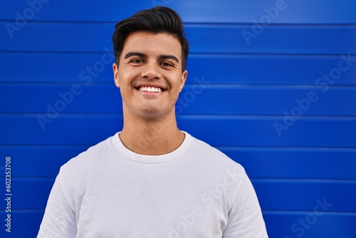 Young hispanic man smiling confident standing over isolated blue background