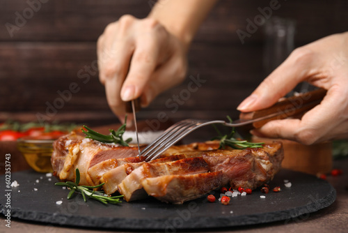 Woman eating delicious fried meat with rosemary and spices at table, closeup