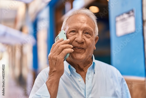 Senior grey-haired man smiling confident talking on the smartphone at street