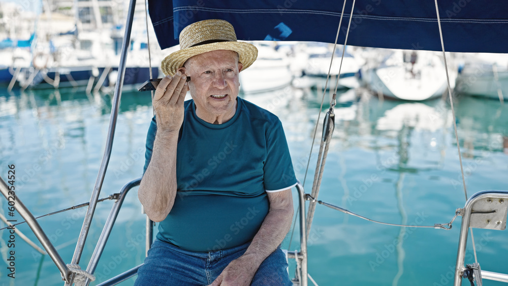 Senior grey-haired man tourist wearing summer hat listening voice message by smartphone at boat