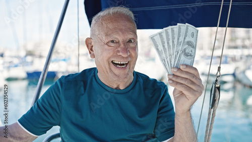 Senior grey-haired man smiling confident holding dollars at boat