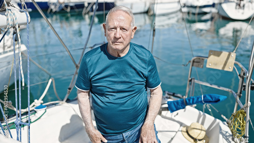 Senior grey-haired man standing with relaxed expression at boat
