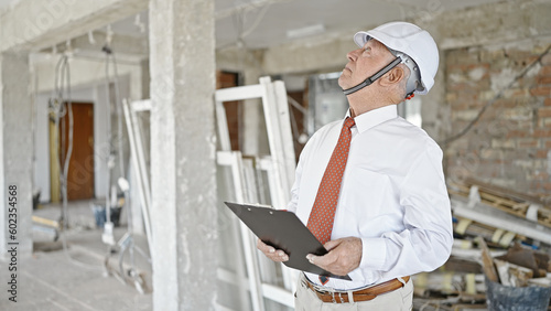 Senior grey-haired man architect holding clipboard looking around at construction site © Krakenimages.com