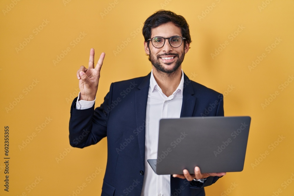 Handsome latin man working using computer laptop smiling looking to the camera showing fingers doing victory sign. number two. Handsome latin man working using computer laptop smiling looking to the camera showing fingers doing victory sign. number two.