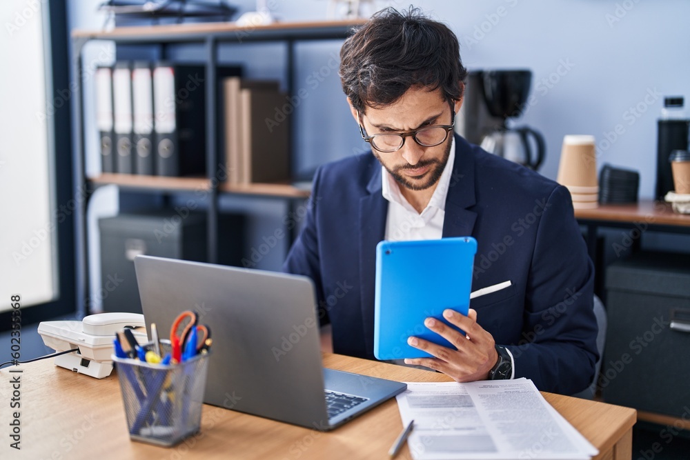 Young hispanic man business worker using laptop and touchpad working at office Young hispanic man business worker using laptop and touchpad working at office