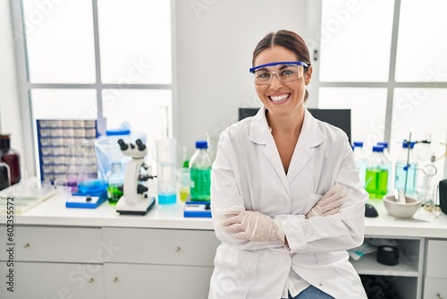 Young beautiful hispanic woman scientist smiling confident sitting with arms crossed gesture at laboratory