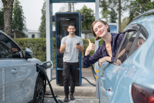 White woman show thumb up to camera with little smile at Electral car add fluel station, saving money and world with good qualiti of green energy. photo