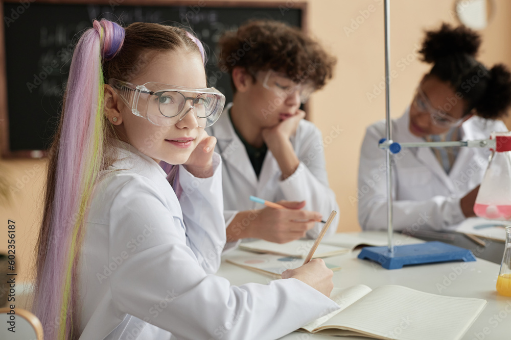 Portrait of cute schoolgirl with pigtails enjoying science class and looking at camera, copy space