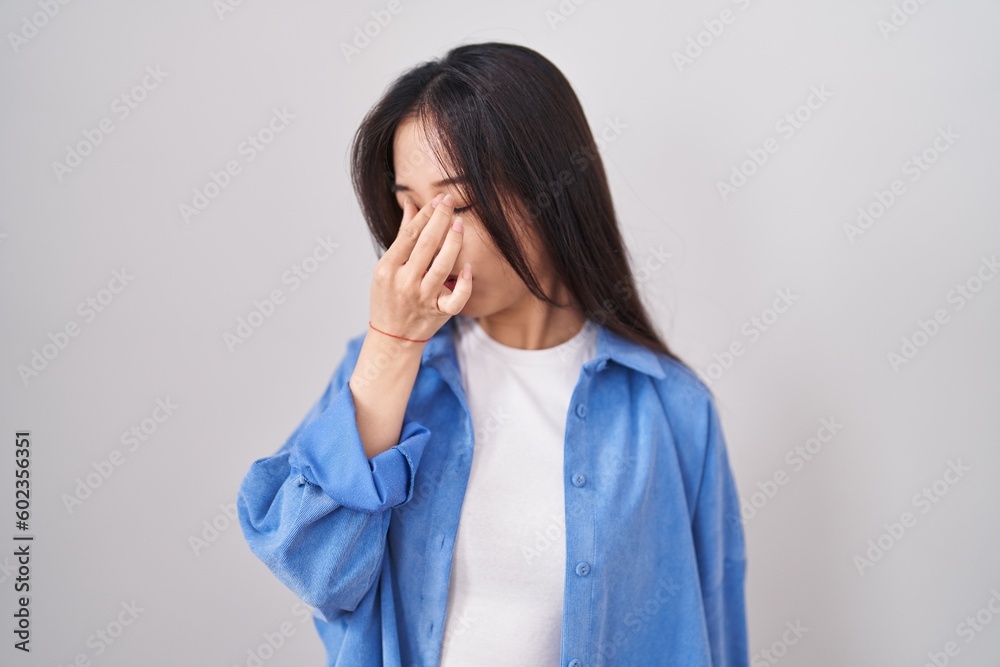 Young chinese woman standing over white background tired rubbing nose and eyes feeling fatigue and headache. stress and frustration concept. Young chinese woman standing over white background tired rubbing nose and eyes feeling fatigue and headache. stress and frustration concept.