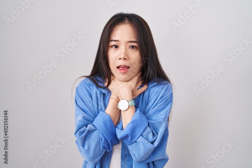 Young chinese woman standing over white background shouting suffocate because painful strangle. health problem. asphyxiate and suicide concept.