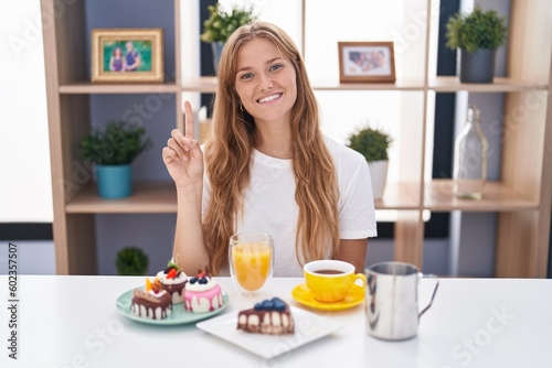 Young caucasian woman eating pastries t for breakfast showing and pointing up with finger number one while smiling confident and happy.