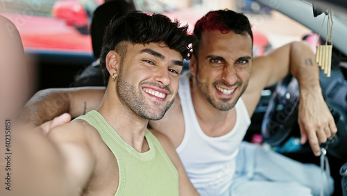Two men couple make selfie by smartphone sitting on car at street