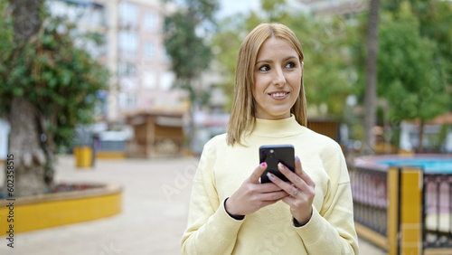 Young blonde woman smiling confident using smartphone at park