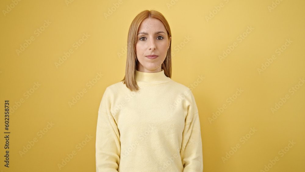 Young blonde woman standing with relaxed expression over isolated yellow background Young blonde woman standing with relaxed expression over isolated yellow background