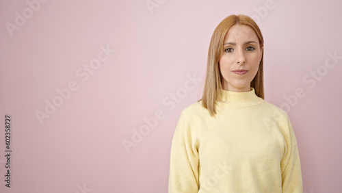 Young blonde woman standing with relaxed expression over isolated pink background