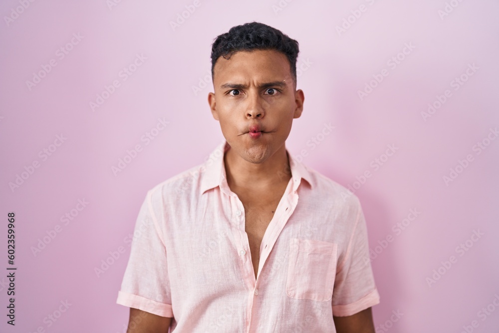 Young hispanic man standing over pink background making fish face with lips, crazy and comical gesture. funny expression. Young hispanic man standing over pink background making fish face with lips, crazy and comical gesture. funny expression.