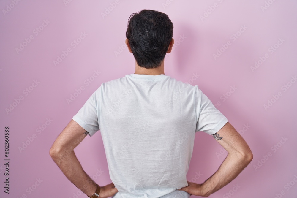 Obraz premium Young hispanic man standing over pink background standing backwards looking away with arms on body