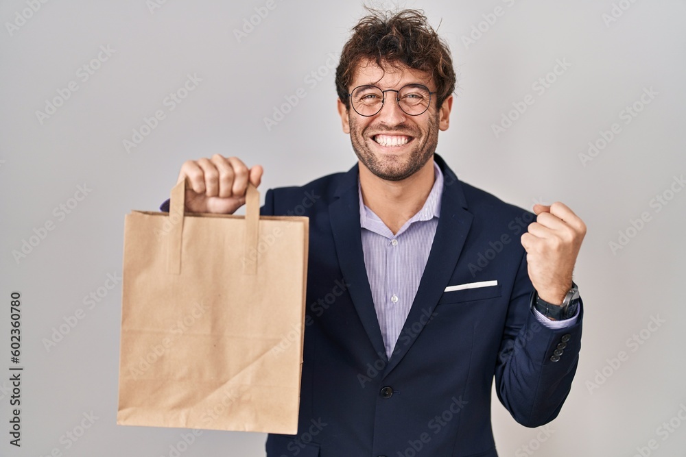 Hispanic business man holding delivery bag screaming proud, celebrating victory and success very excited with raised arms Hispanic business man holding delivery bag screaming proud, celebrating victory and success very excited with raised arms