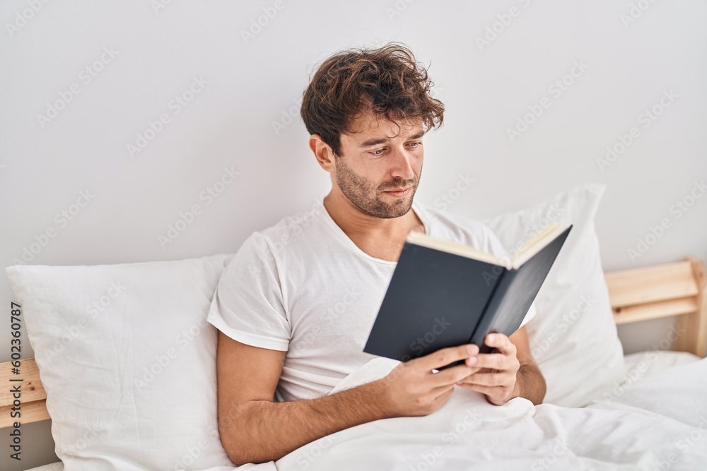 Young man reading book sitting on bed at bedroom Young man reading book sitting on bed at bedroom